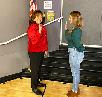 Woman in red smiling while being sworn in by another woman