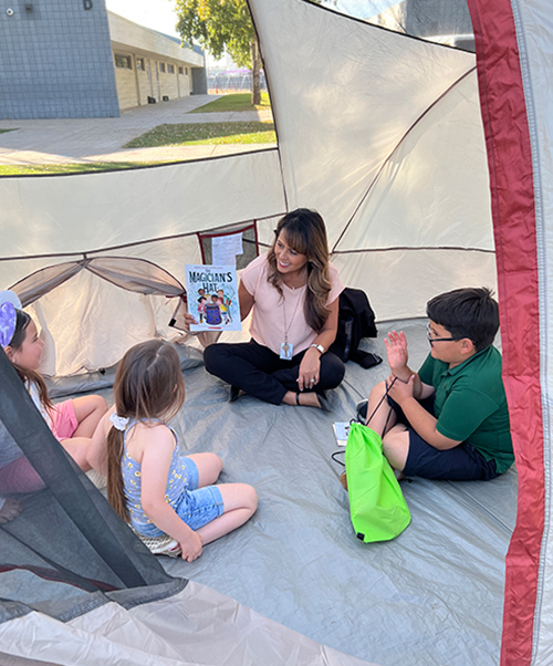 Superintendent Herrera reading with students in a tent on campus